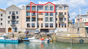 Een gebouw aan het water met meerdere verdiepingen, balkons en een steiger met boten.