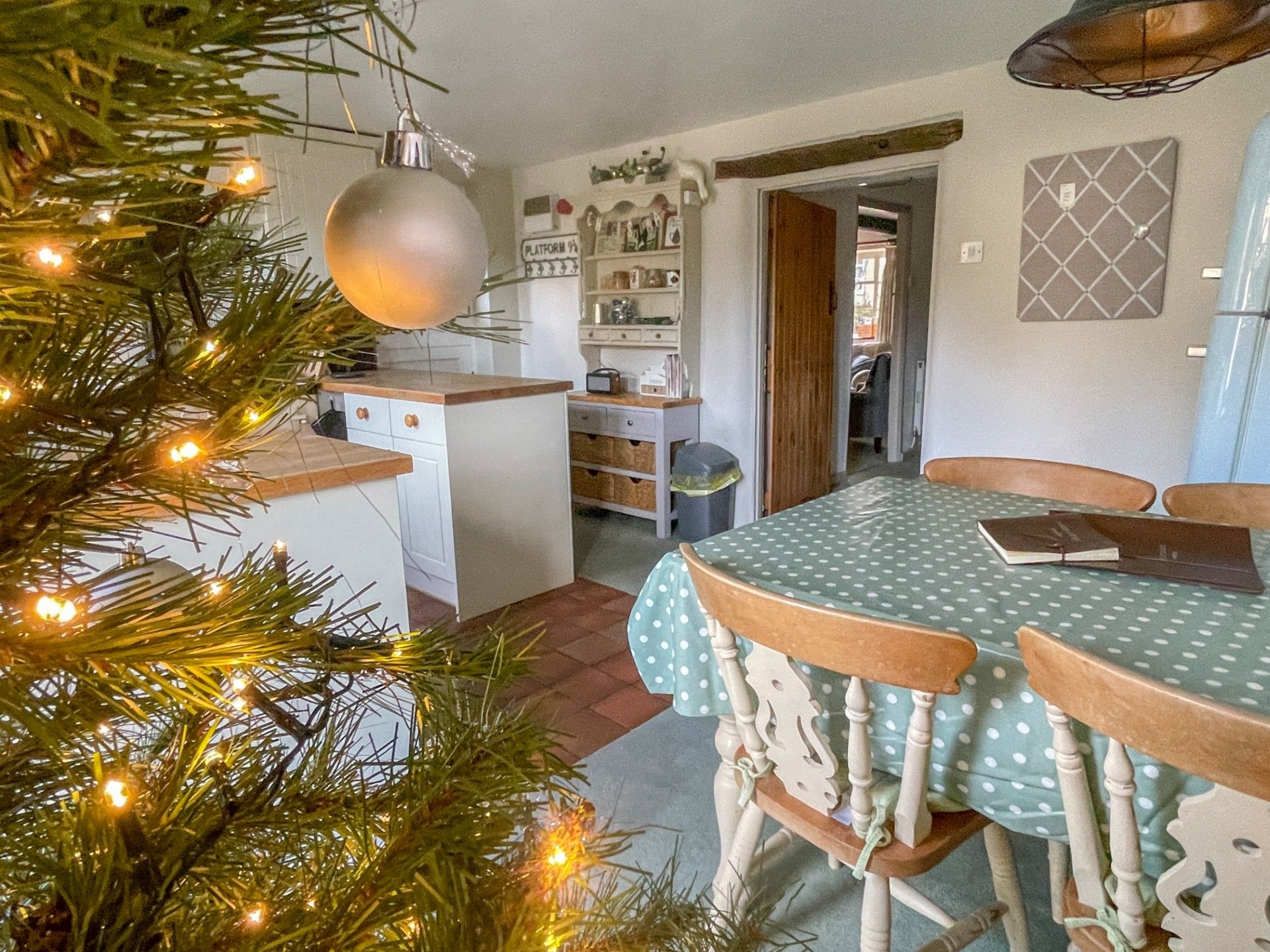 A kitchen with a dining table and chairs, a Christmas tree with lights, and a hallway leading to another room.