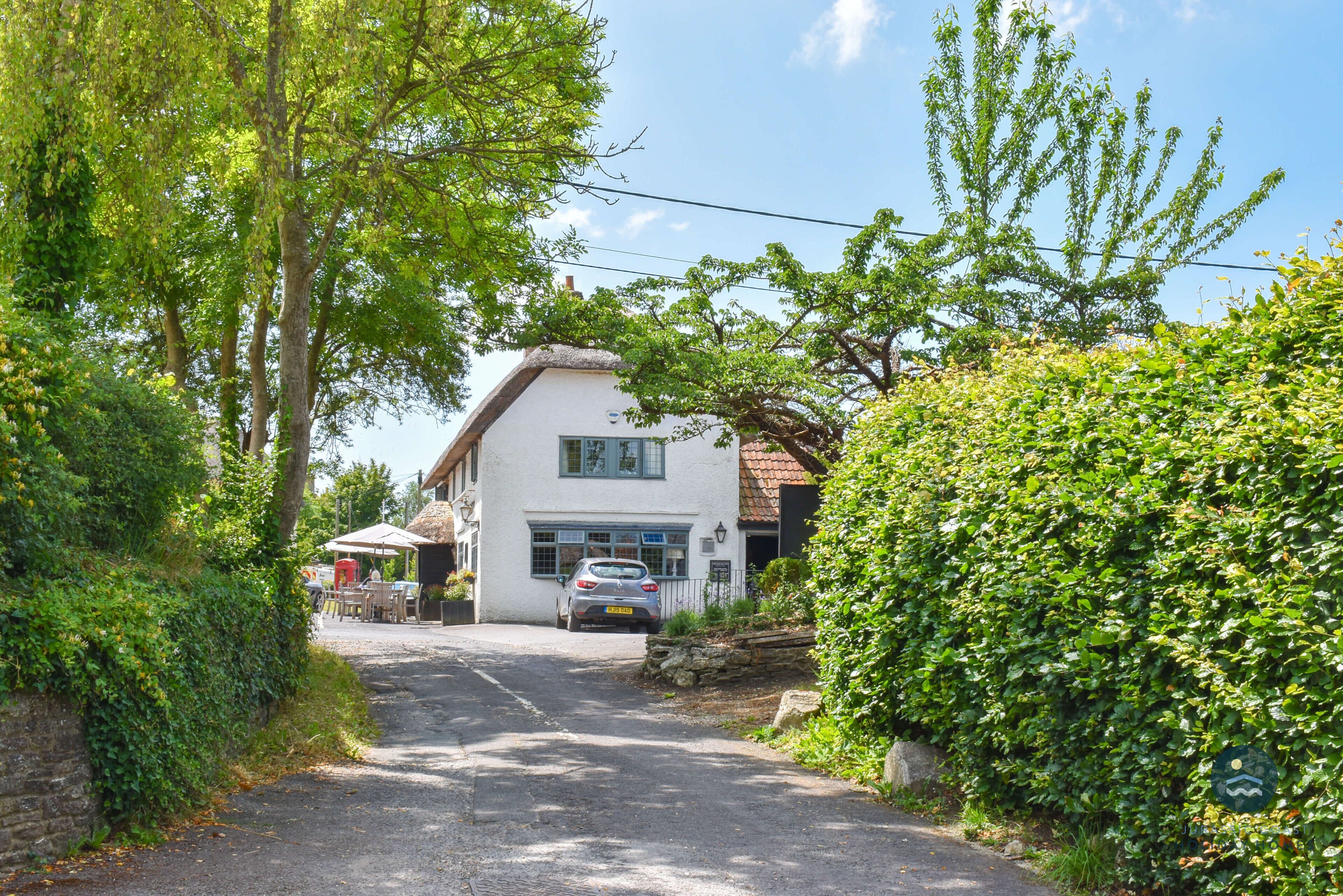 A white building with a thatched roof, a paved driveway, and a car parked in front.