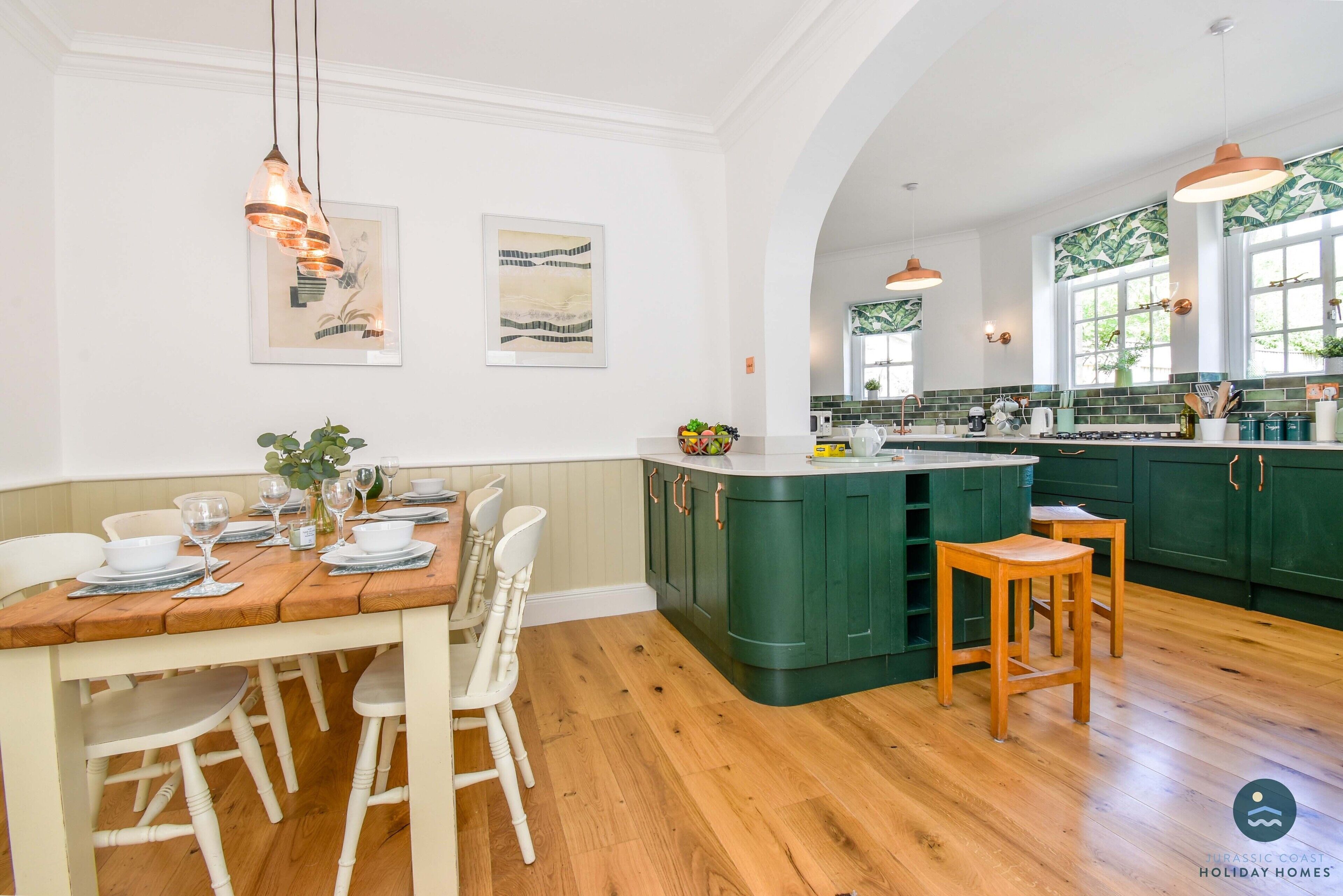 A kitchen with wooden flooring, green cabinets, and pendant lighting.