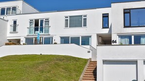 A modern two-story building with a flat roof, large windows, and a grassy front. - Pebble House - Sea views, parking, family friendly (Weymouth)