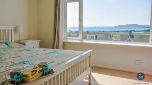 A bedroom with a bed, a window with a view of the sea, and a tray with tea bags and mugs. - Pebble House - Sea views, parking, family friendly (Weymouth)