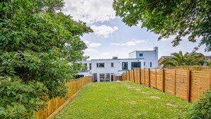 A modern house with a white exterior, a wooden fence, and a well-maintained lawn. - Pebble House - Sea views, parking, family friendly (Weymouth)
