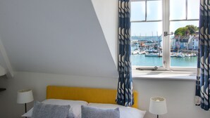 A hotel room with a bed, a window with curtains, a view of a marina, and a lamp on the side table. - Quay View Apartment - Four Bedroom Apartment, Sleeps 8 (Weymouth)
