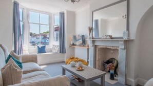 A cozy living room with a fireplace, comfortable seating, and a view of the outside. - Quay View Apartment - Four Bedroom Apartment, Sleeps 8 (Weymouth)