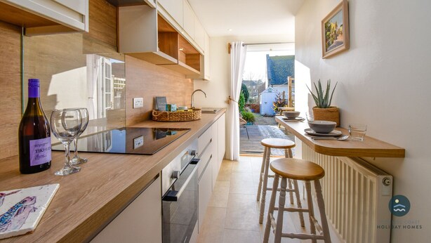 Une cuisine moderne avec un plan de travail en bois, une bouteille de vin et des verres. On aperçoit un jardin à travers une porte ouverte.