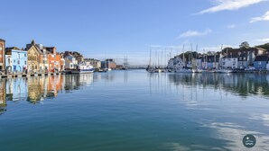 Un port de plaisance avec des bateaux amarrés, des bâtiments le long de la rive et un ciel dégagé.