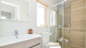 A modern bathroom with a glass-enclosed shower, a white sink, and a toilet.