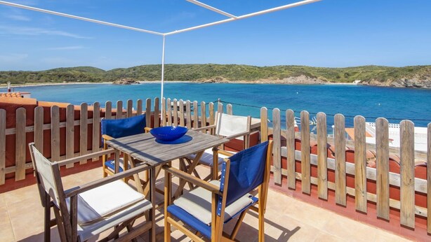 A terrace with a table and chairs, overlooking a coastal view.