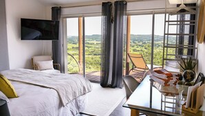 Een slaapkamer met een groot bed, een tv aan de muur, een balkon met een stoel en een tafel met handdoeken en een wereldbol.