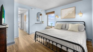 Un dormitorio con cama, mesita de noche, lámpara de pared, cuadro enmarcado y ventana con vistas.