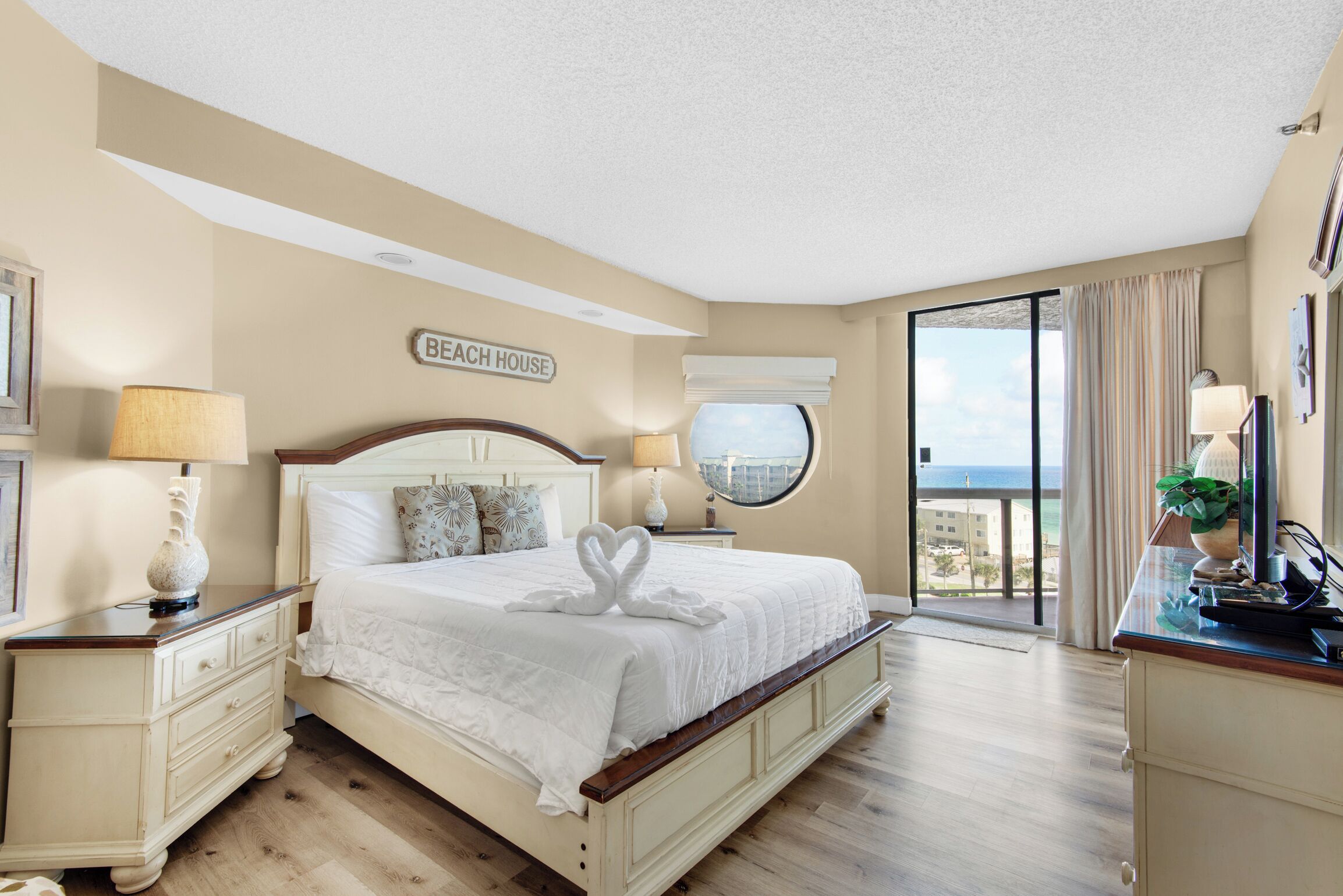 A hotel room with a large bed, a view of the beach, and a sign that reads "Beach House".