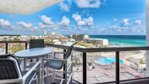 A balcony with a view of a beach and pool area, including lounge chairs and a table. - 🌊Gulf Views-Beach Service for Two-Pool-Tiki Bar-2BR Surfside Resort #505🌊 (Miramar Beach)