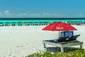 A beach with lounge chairs and umbrellas, a sign advertising ice cold beer, and the ocean in the background.