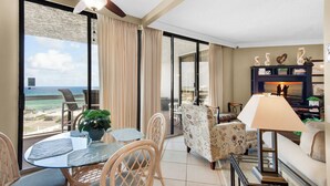 A spacious living area with a balcony overlooking the beach, furnished with a glass table, chairs, and a sofa. - 🌊Gulf Views-Beach Service for Two-Pool-Tiki Bar-2BR Surfside Resort #505🌊 (Miramar Beach)