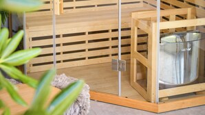 A sauna with wooden benches and glass doors, a wooden bench with a towel, and a sauna heater visible. - Les Hauts d'Avignon - Guesthouse - Room 1 (Rochefort-du-Gard)