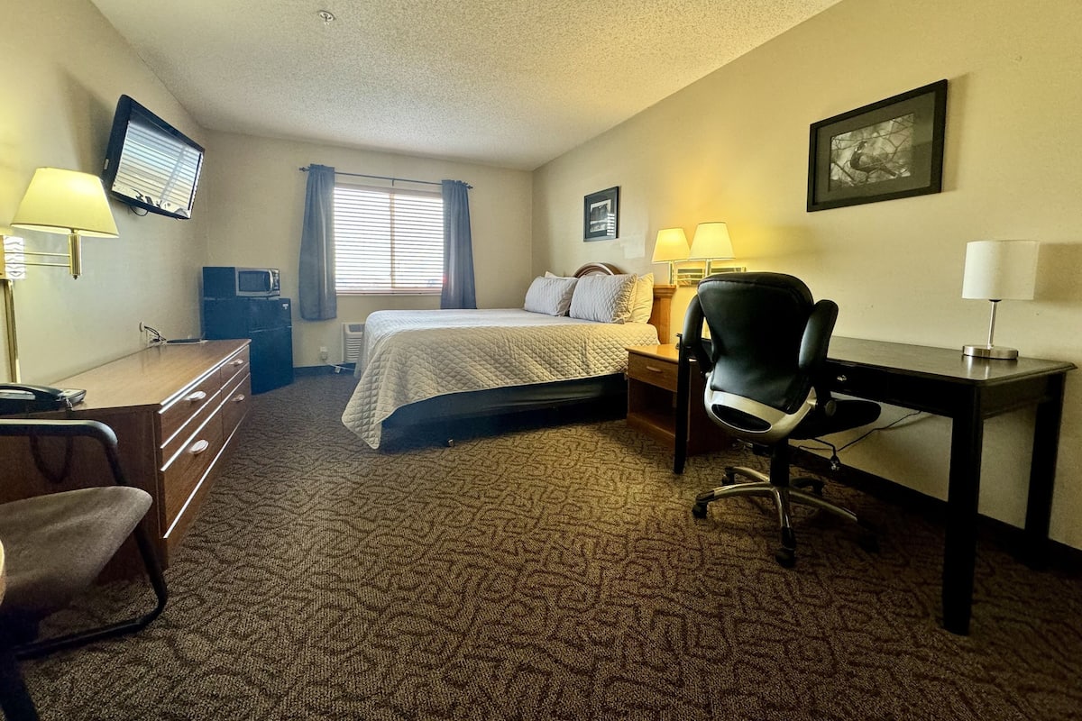 A hotel room with a bed, desk, chair, and a television on the wall.