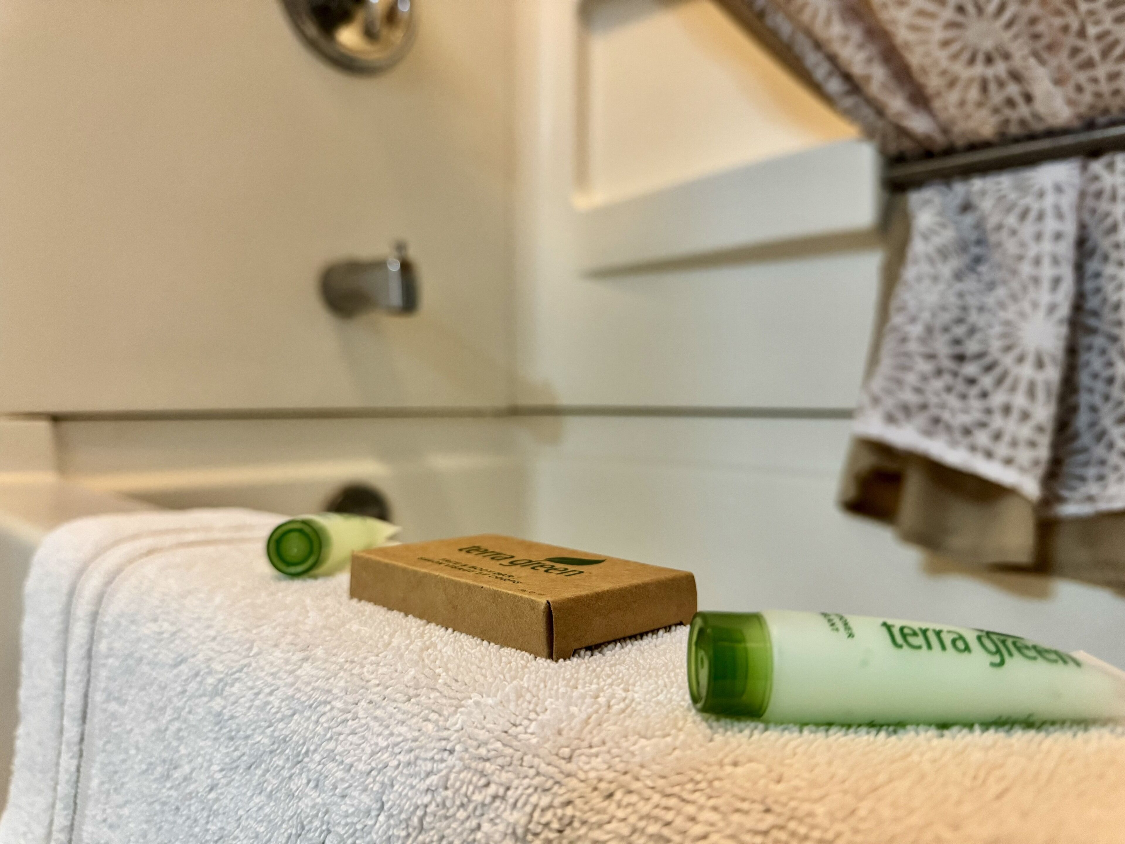 Un baño con una toalla blanca, una caja marrón y una botella verde sobre una superficie blanca con textura.