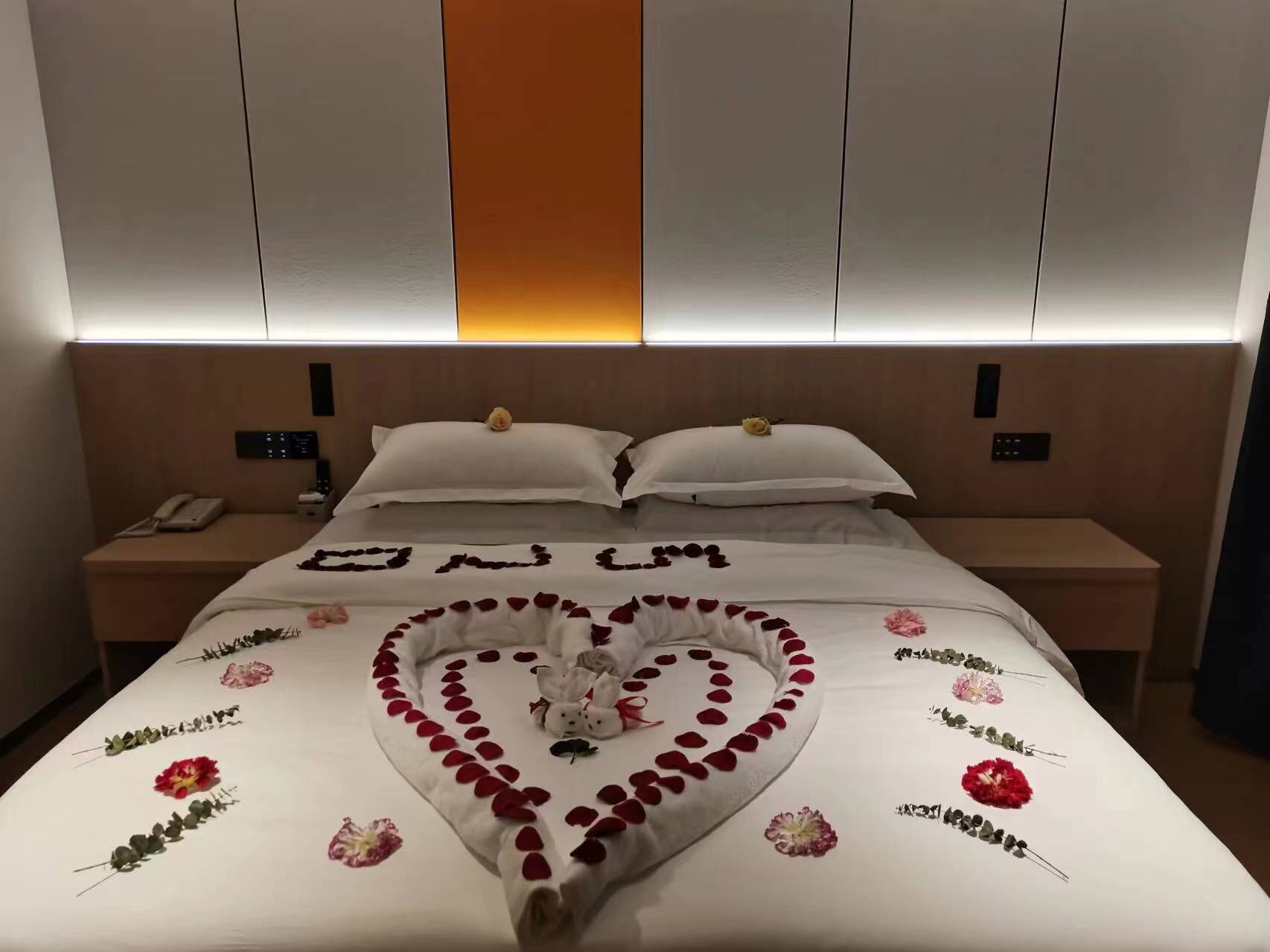 Habitación de hotel con una cama bien hecha, una mesita de noche con un teléfono y un panel de control instalado en la pared.