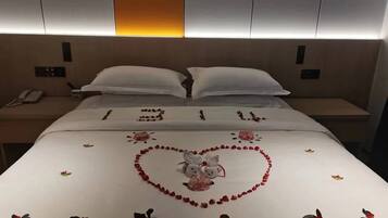 A hotel room with a neatly made bed, a bedside table with a phone, and a wall-mounted control panel.