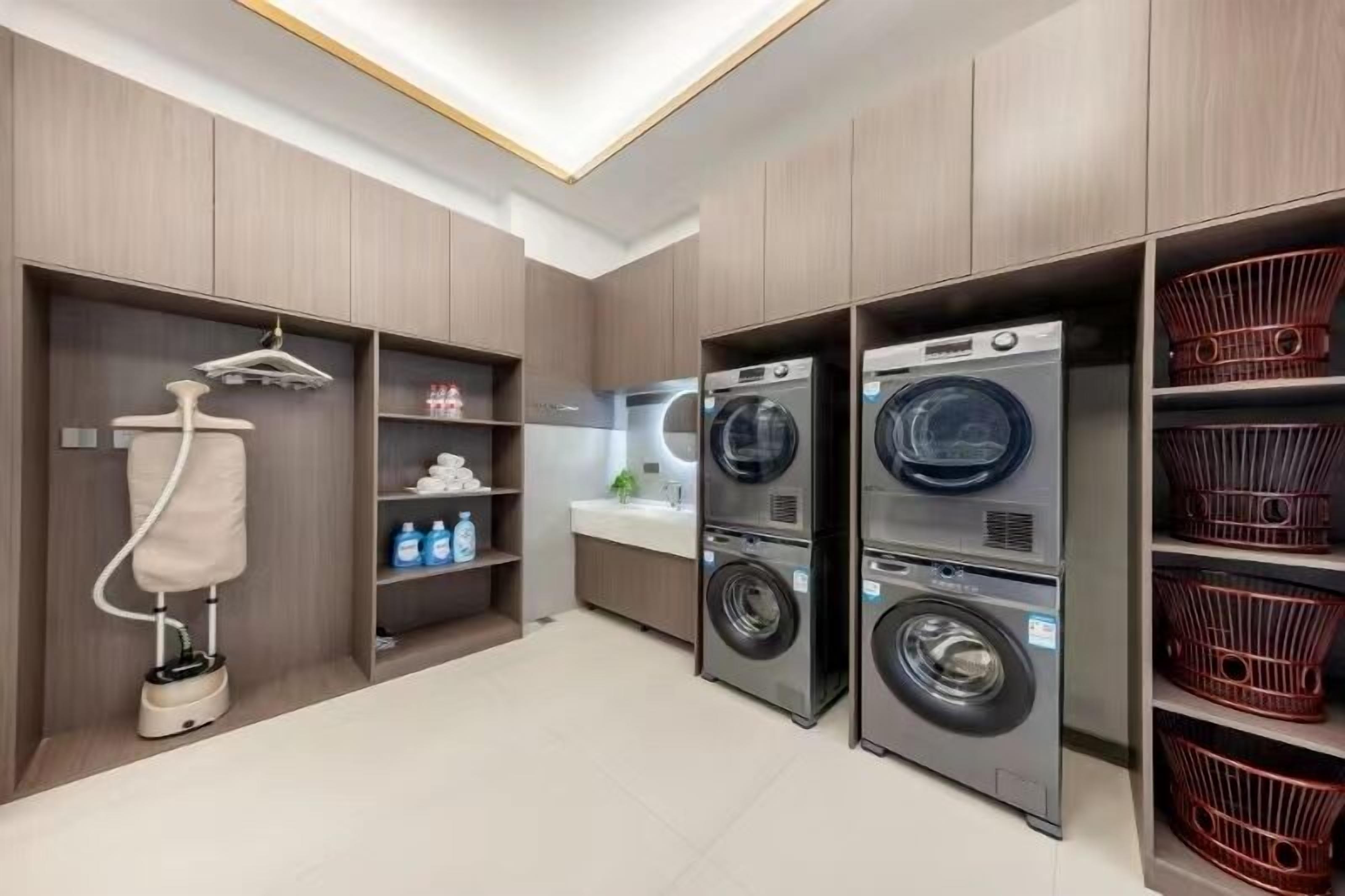 A modern laundry room with built-in washing machines and dryers, a drying rack, and a small sink area.
