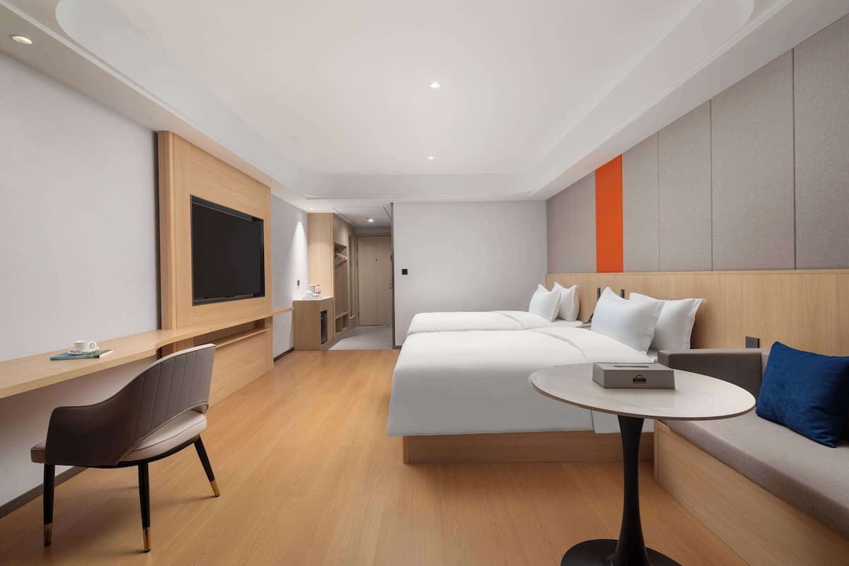 A modern hotel room with a large bed, a desk, a chair, and a TV mounted on the wall.
