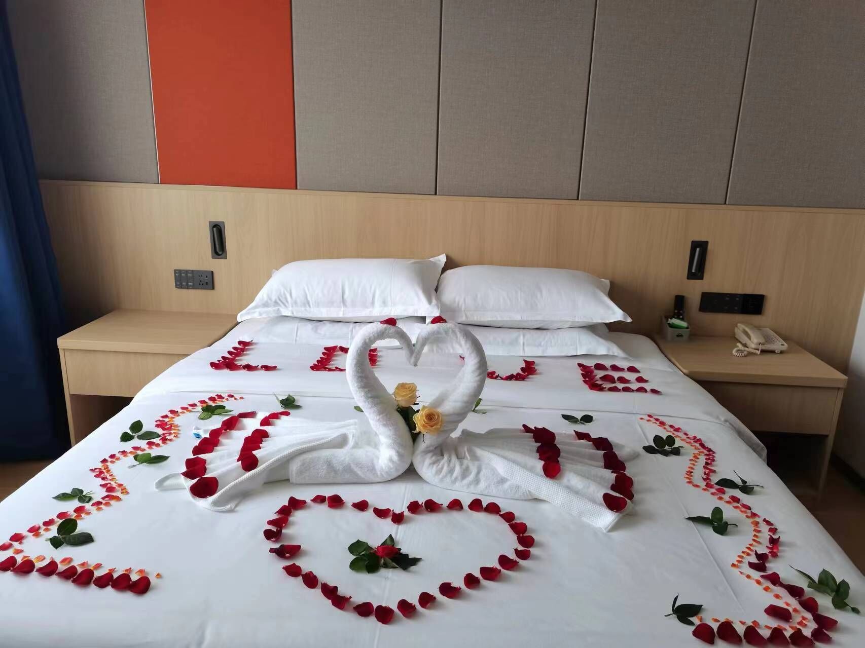 Habitación de hotel con una cama bien hecha, cabecera de madera, mesita de noche con un teléfono y un panel de pared con diseño rojo y gris.