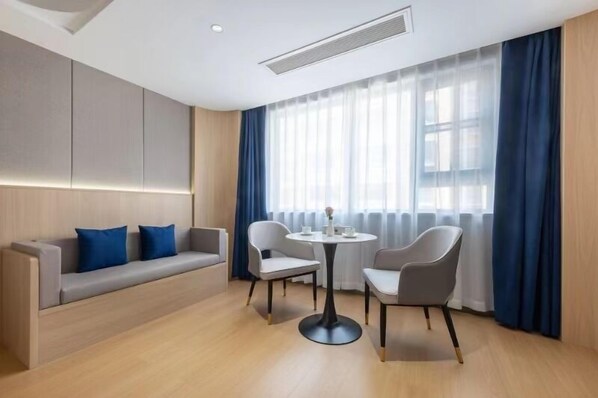 Una habitación de hotel moderna con sofá, dos sillas, una mesita y un ventanal con cortinas.
