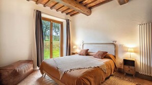 Un dormitorio con una cama grande, vigas de techo de madera, vistas a través de una ventana y una mesita de noche con lámpara.