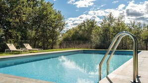 Una piscina rectangular con agua azul cristalina, rodeada por un solárium con baldosas. Se observan dos tumbonas y una escalera metálica en el lado derecho.