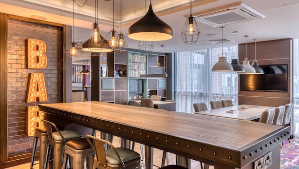 Een moderne keuken met een houten bar, hanglampen en een bakstenen muur met verlichte letters.