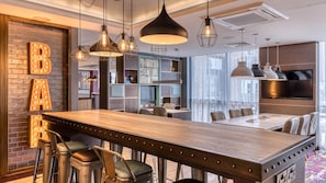 A modern kitchen with a wooden bar, pendant lights, and a brick wall with illuminated letters.