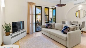 Uma sala de estar moderna com televisão de tela plana, um sofá, um espaço de refeições e uma varanda com vista.