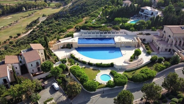 Uma grande piscina rodeada por um jardim bem cuidado, com um campo de golfe ao fundo.
