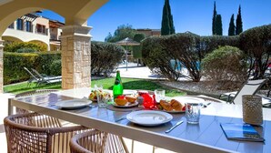 An outdoor dining area with a table set for a meal, surrounded by a view of a well-maintained garden and tall trees.