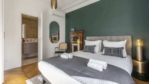 A bedroom with a large bed, a mirror, a fireplace, and a wardrobe. - Sweett | Wagram Deluxe XI (Paris)