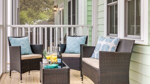 A porch with wicker furniture, a table with a bottle and glasses, and a view of trees. - Stay @ Jasper Jetty - 8 bedrooms, 2 pools! (Folly Beach)
