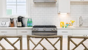 A modern kitchen with white cabinets, a stainless steel range, and a gas stove. There are wicker baskets hanging from the ceiling and a window with blinds. - Stay @ Jasper Jetty - 8 bedrooms, 2 pools! (Folly Beach)