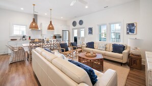 A spacious living area with a sofa, chairs, and a coffee table. There is a dining area with a table and chairs, and a kitchen in the background. - Stay @ Jasper Jetty - 8 bedrooms, 2 pools! (Folly Beach)