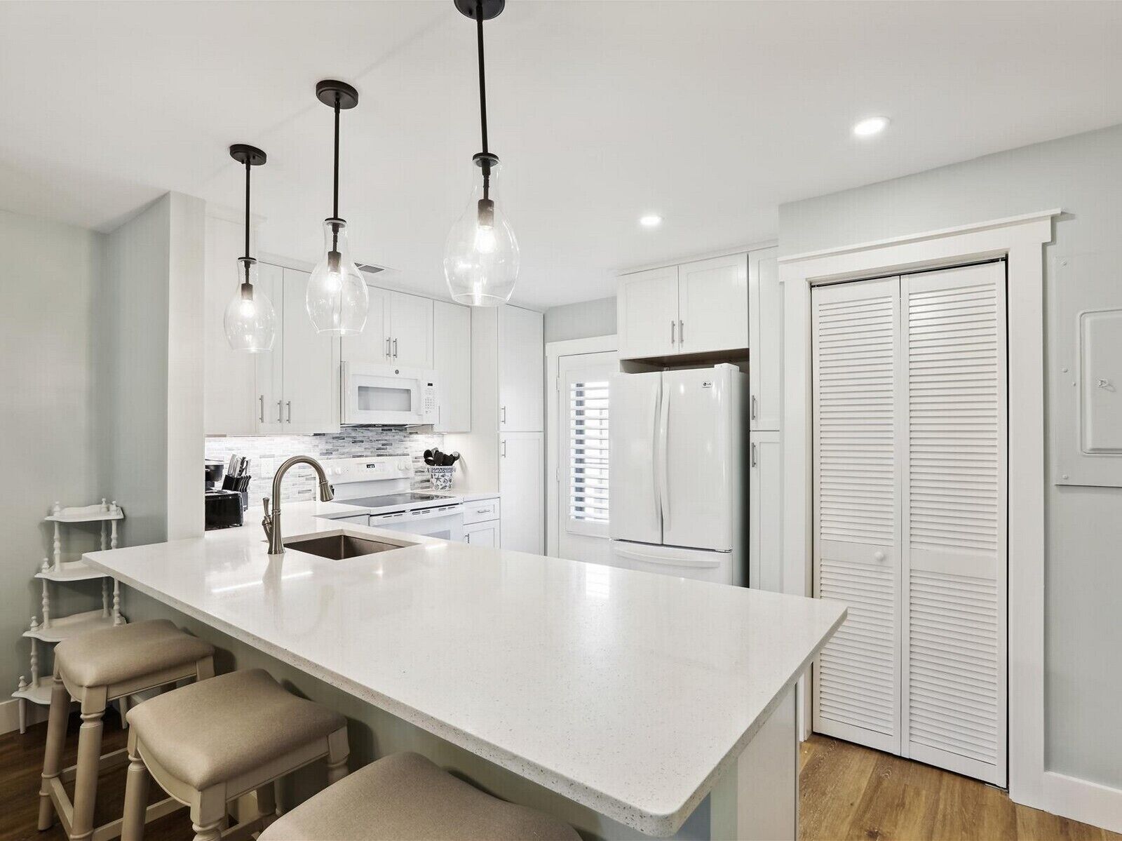 A modern kitchen with a large island, white cabinetry, a refrigerator, and pendant lighting.