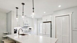 Eine moderne Küche mit einer großen Kochinsel, weißen Schränken, einem Kühlschrank und Pendelleuchten.