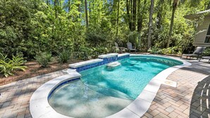 A swimming pool with a curved edge, surrounded by a brick patio and lush greenery. - Single Level Vacation Home w/ Private Pool (Hilton Head Island)