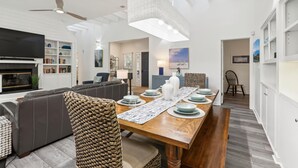A modern living room with a sofa, a dining table set for four, and a TV in the background. - Single Level Vacation Home w/ Private Pool (Hilton Head Island)