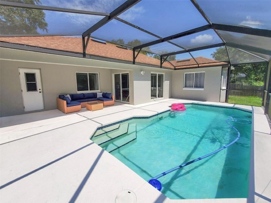 Piscina coberta ao ar livre com área de estar integrada e uma casa ao fundo.