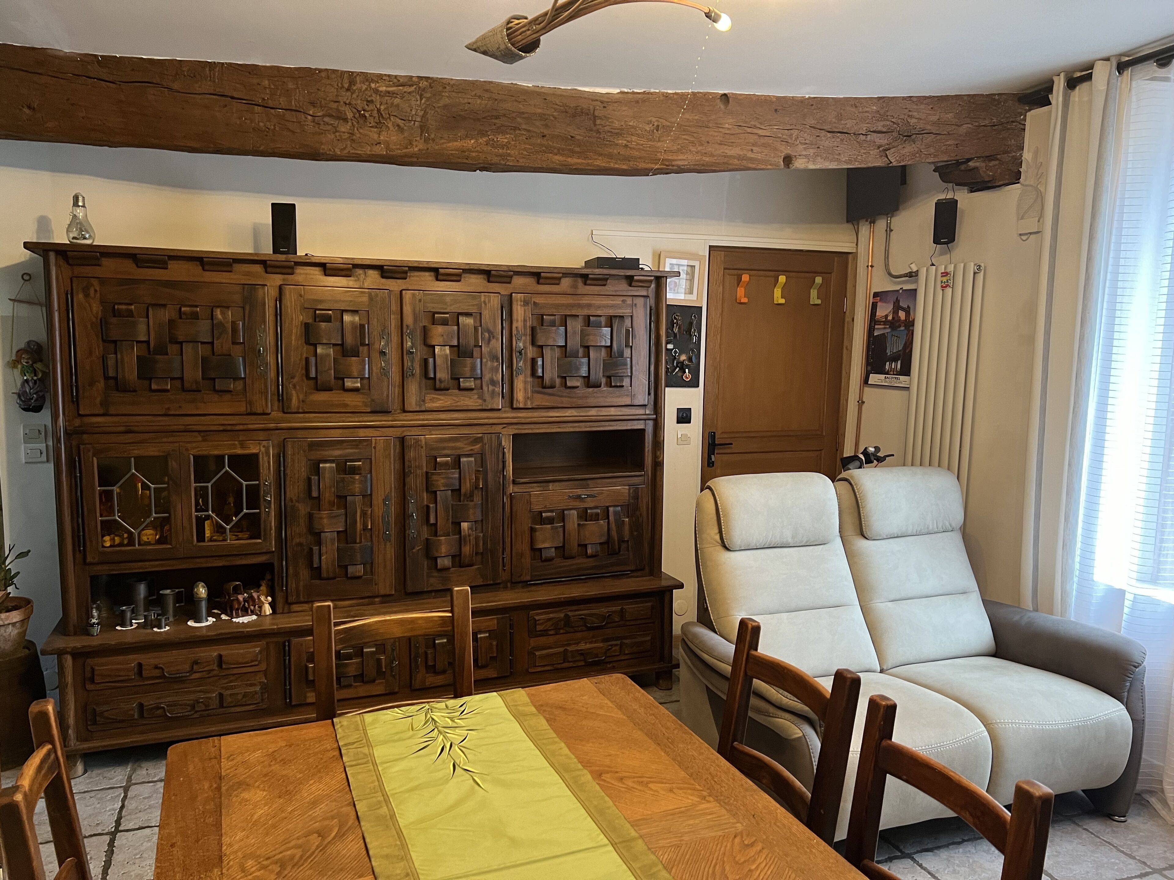 A dining area with a wooden table and chairs, a built-in wooden cabinet with glass doors, a beige armchair, and a ceiling light fixture.