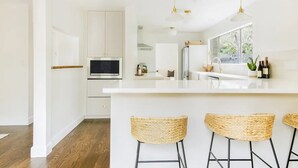 Eine moderne Küche mit weißen Schränken, einem Edelstahlbackofen, einer großen Kochinsel mit Barhocker und hängenden Pendelleuchten.