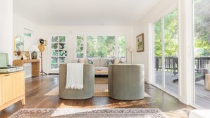 Ein geräumiges Wohnzimmer mit großem Fenster, einer Couch, zwei Sesseln, einer Holzkommode und einem Teppich.