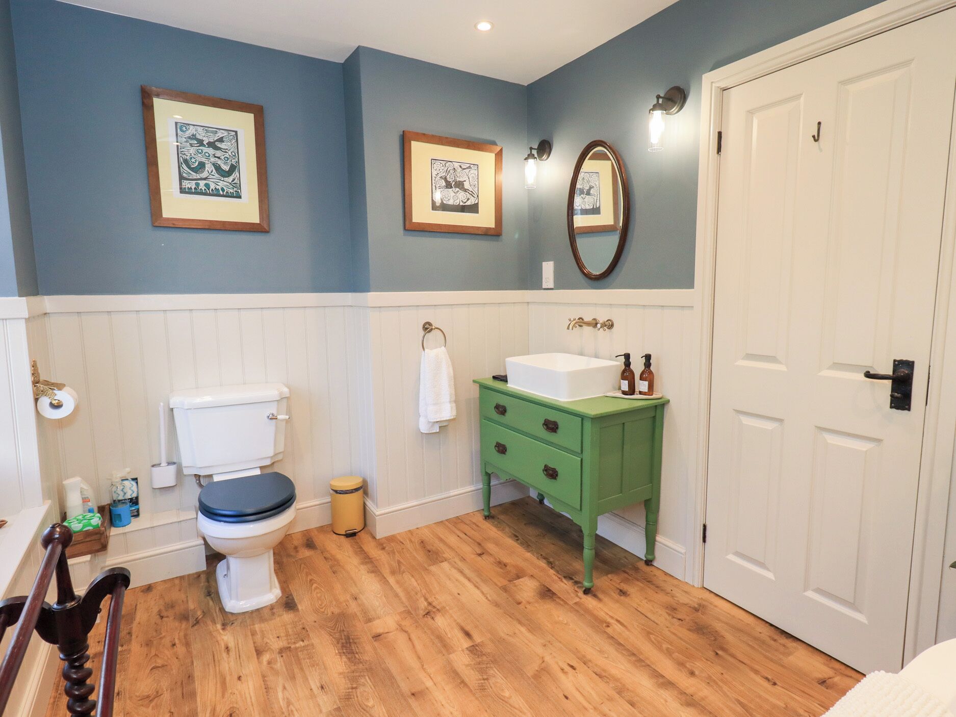 Une salle de bain équipée de toilettes, d’un lavabo et d’œuvres d’art encadrées accrochées aux murs.