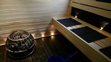 Una habitación con piso de madera, una parrilla de carbón, un balde azul y una cama con cabecera.