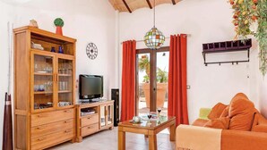 Ein Wohnzimmer mit einem Holzkasten, einem Fernseher, einem Tisch mit Glasplatte und einem Sofa.